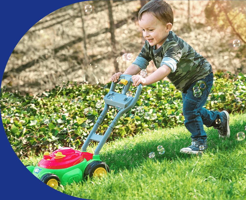 Toddler pushing a Maxx Bubbles bubble mower across the lawn